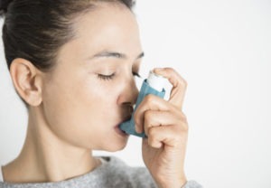 Young woman inhaling asthma inhaler, close-up.