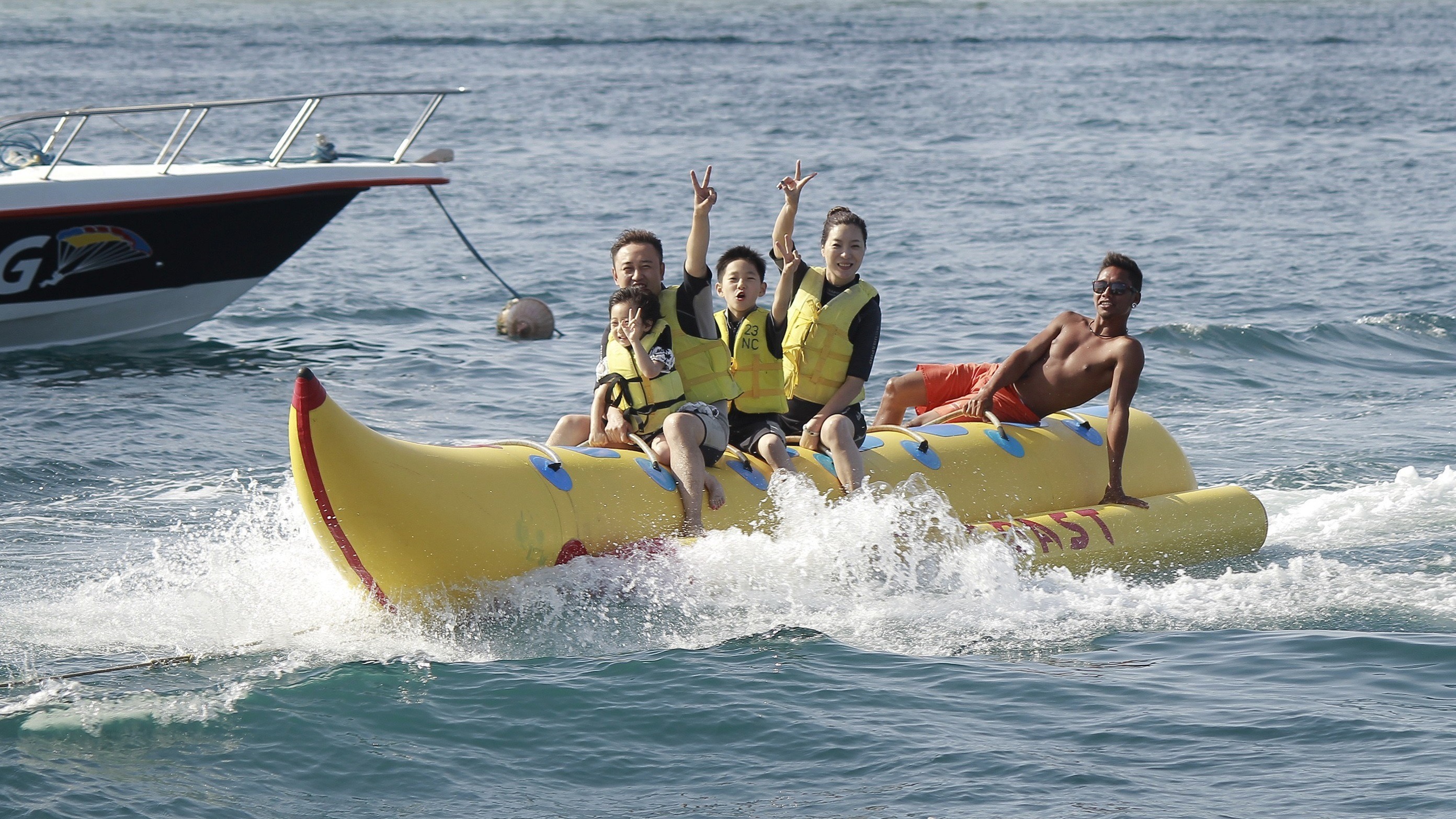 three adults two kids riding inflatable banana boat