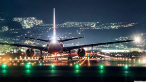 plane landing on airport with a light up city in the night