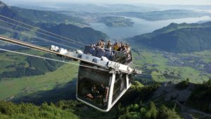 mountain cable car carrying people going up a mountain, view of lake and mountains